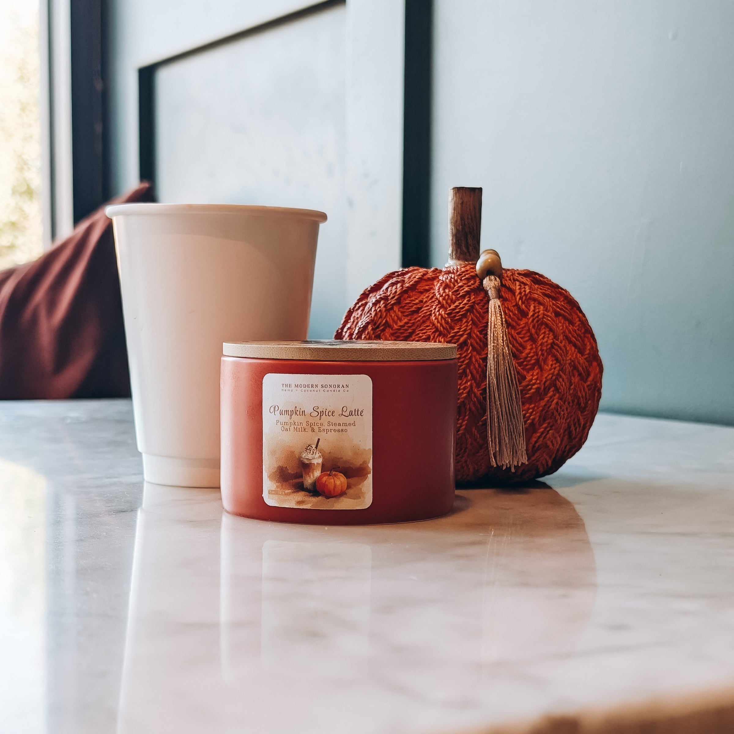 Candle labeled 'Pumpkin Spice Latte' on a table with a decorative pumpkin and plant pot.
