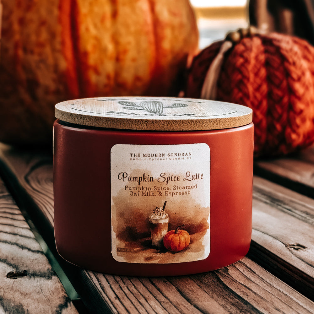 Candle labeled 'Pumpkin Spice Latte' on a wooden surface with pumpkins in the background