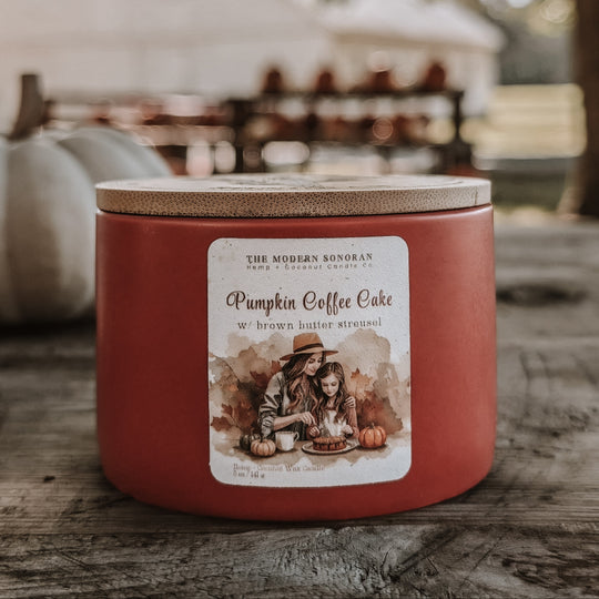 Red candle labeled 'Pumpkin Coffee Cake' on a wooden surface with blurred background