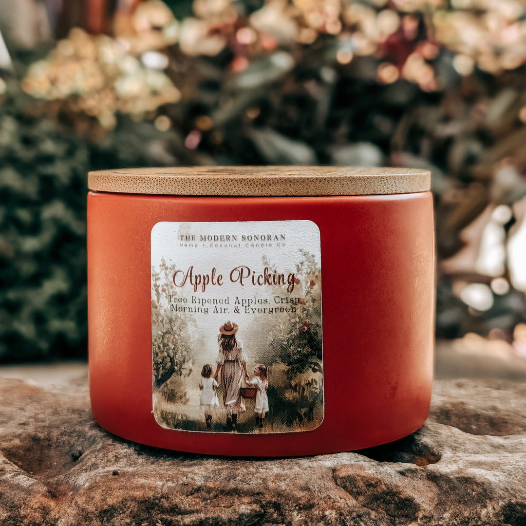 Red candle with a label on a stone surface, surrounded by blurred natural elements
