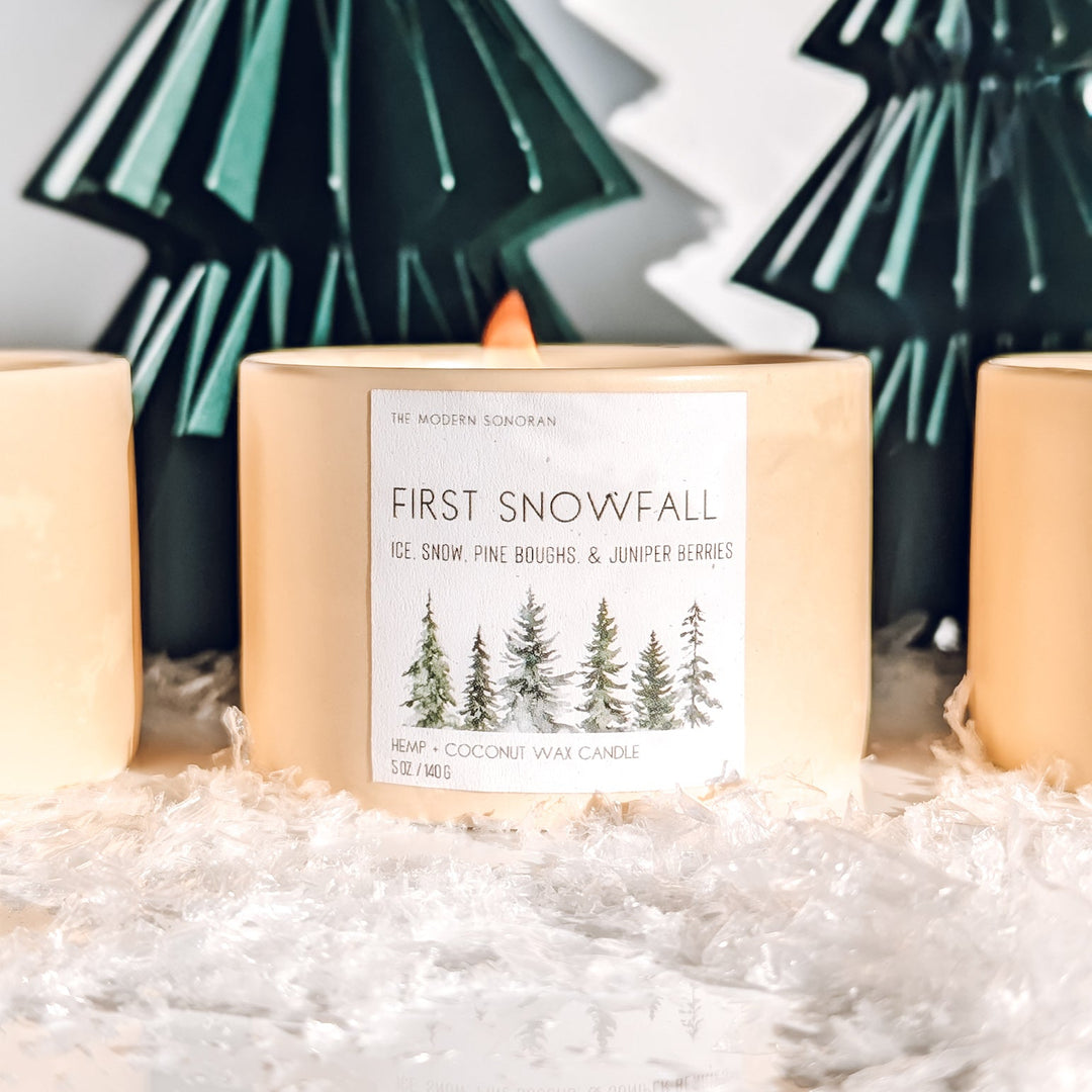 Candle labeled 'First Snowfall' with decorative trees in the background