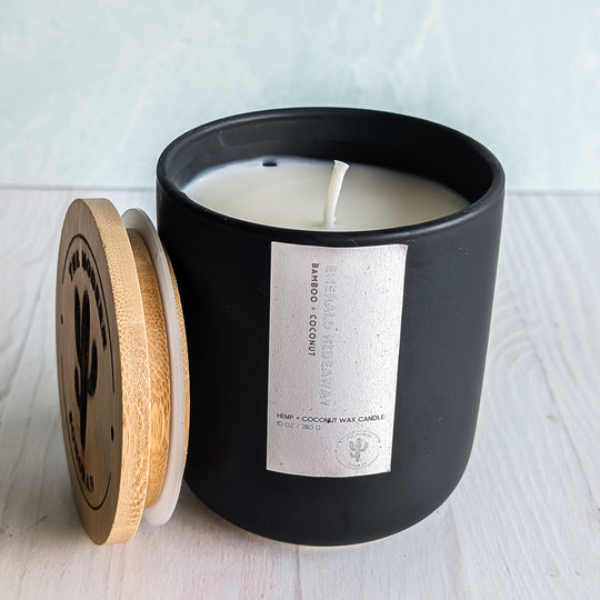 A Emerald Hideaway candle in a black ceramic jar on a table