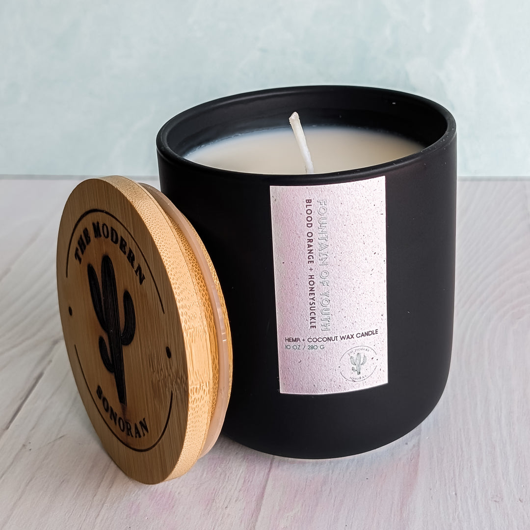A Fountain of Youth candle in a Black ceramic jar on a table with a really boring and empty background.